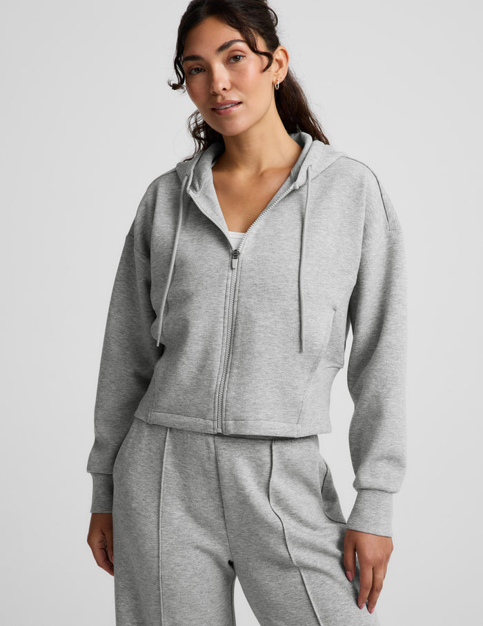 Woman wearing a gray zip-up sweatshirt and gray wide leg pants against a plain background.
