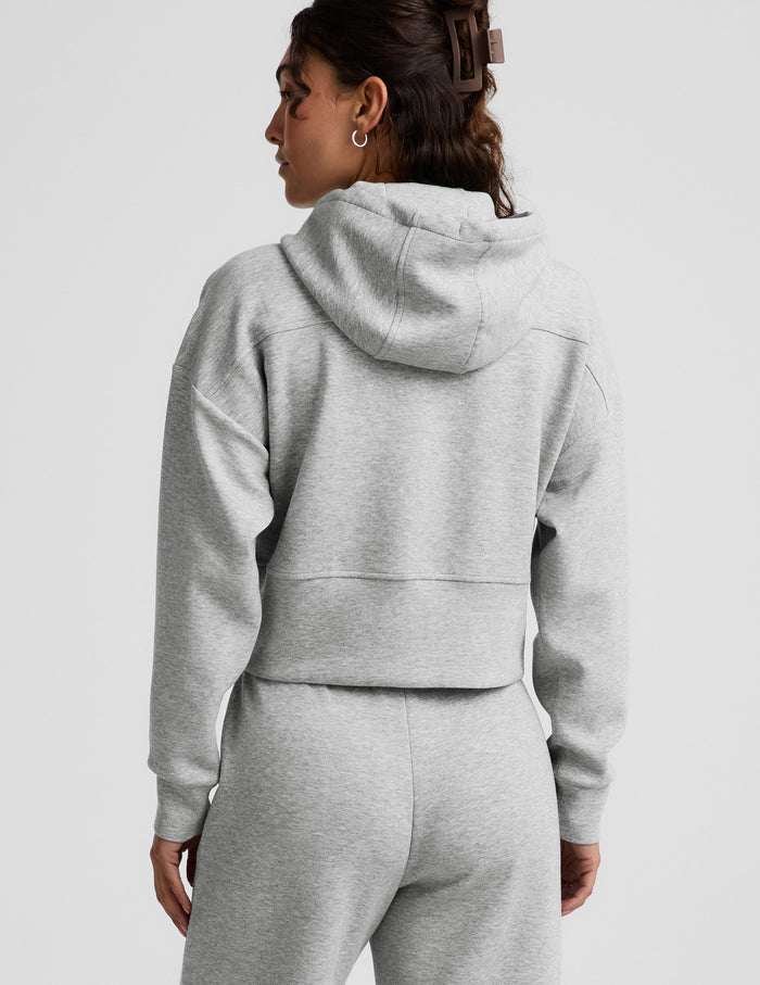 Woman wearing a gray zip-up sweatshirt and gray wide leg pants against a plain background.