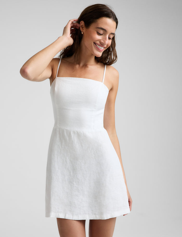 Woman wearing a white linen mini dress against a plain background.