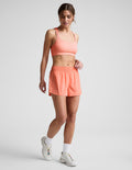 Woman wearing Coral Solemate™ 2.5" Short with a gathered waistband, paired with a matching sports bra and sneakers.