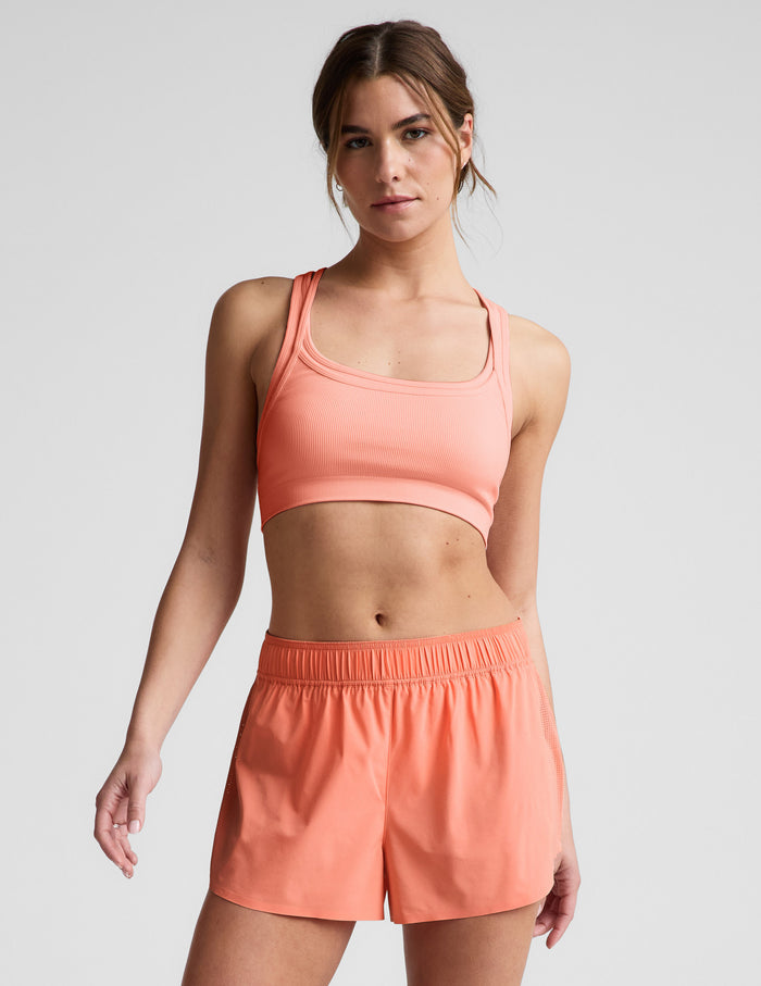 Woman wearing Orange Solemate™ 2.5" Short with perforated side panels, paired with a matching ribbed sports bra.