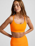 Woman wearing an orange strappy bra and orange leggings against a plain background.