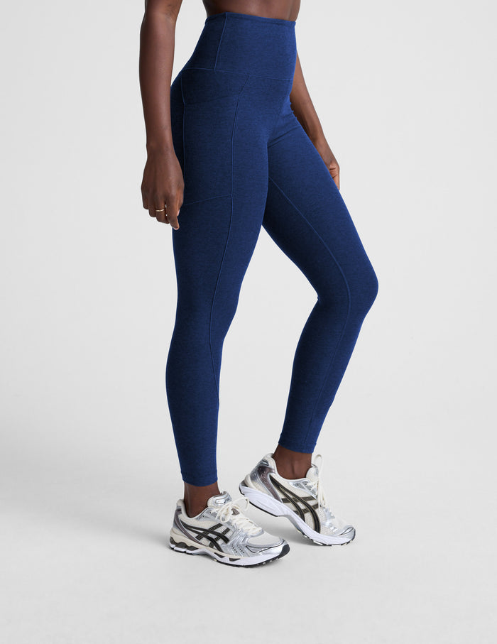 Woman wearing blue high-waisted midi leggings with pockets against a plain background.