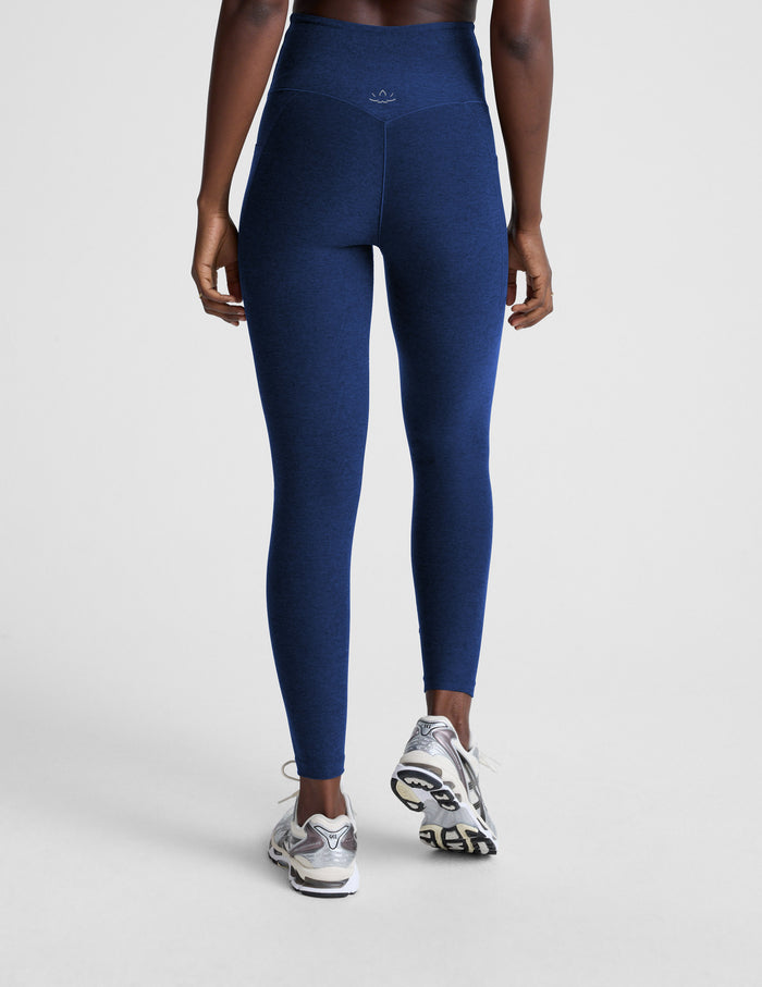 Woman wearing blue high-waisted midi leggings with pockets against a plain background.