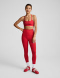 Woman wearing a red racerback sports bra and high-waisted midi length leggings against a plain background.