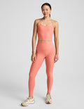Woman wearing a coral cropped tank and leggings set on a gray background.