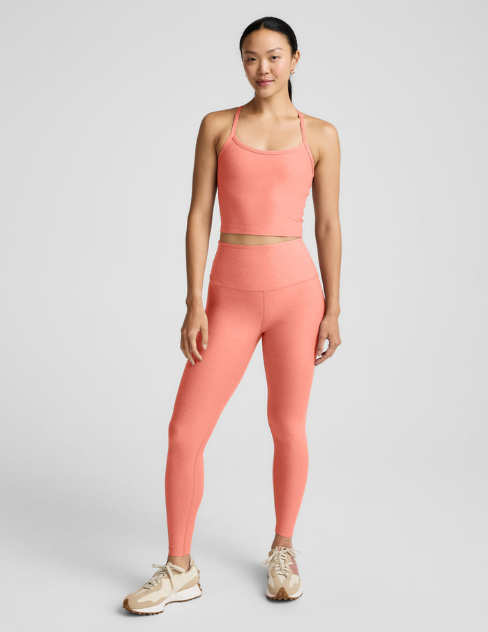 Woman wearing a coral cropped tank and leggings set on a gray background.