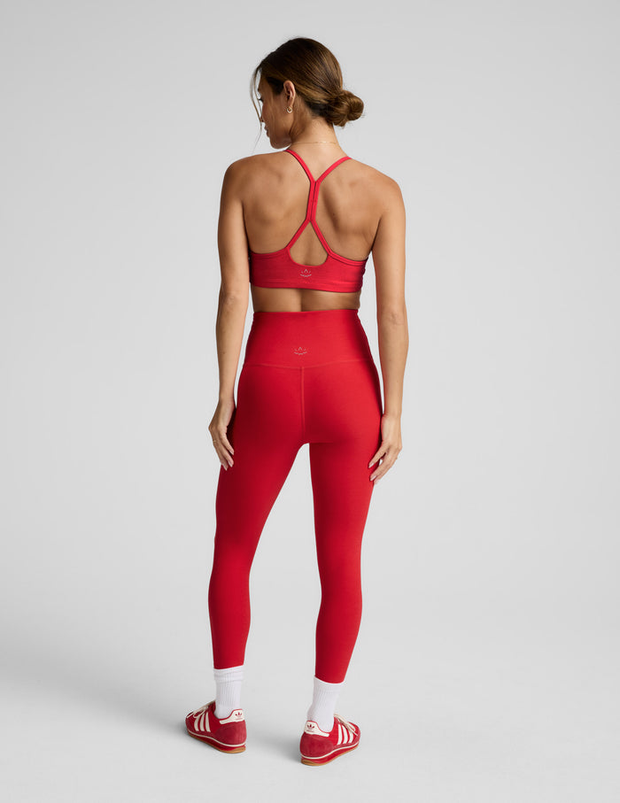 Woman wearing a red racerback sports bra and high-waisted midi length leggings against a plain background.