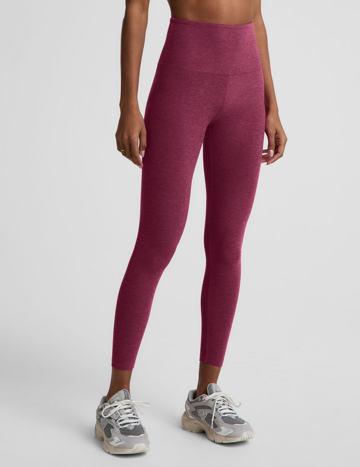 A model wearing high-waisted heathered burgundy leggings and gray athletic sneakers, shown from the waist down against a light gray studio background.