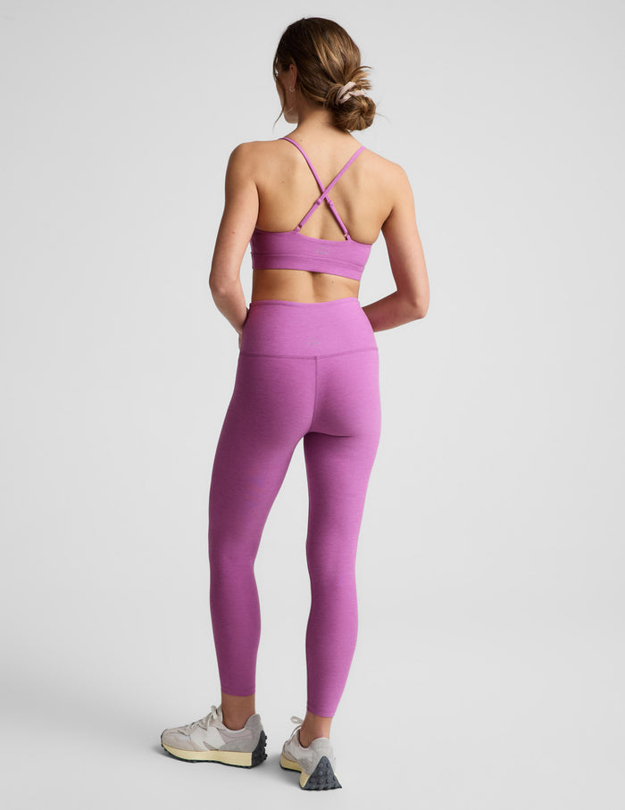 Woman wearing a purple sports bra and leggings on a light gray background.