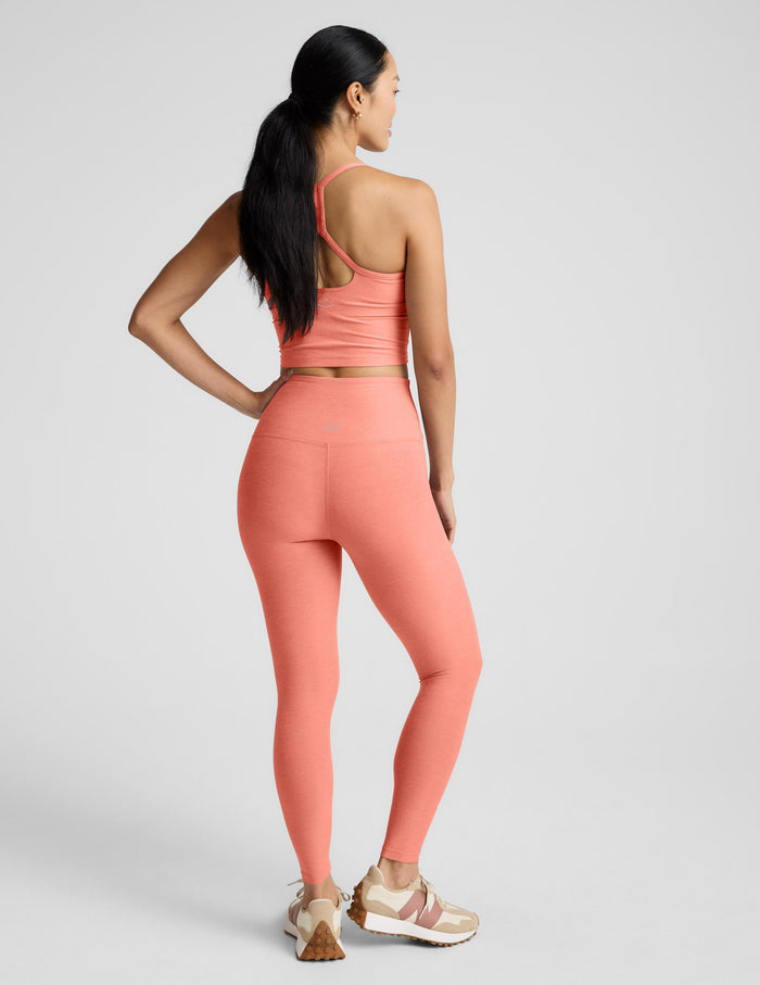 Woman wearing a coral cropped tank and leggings set on a gray background.