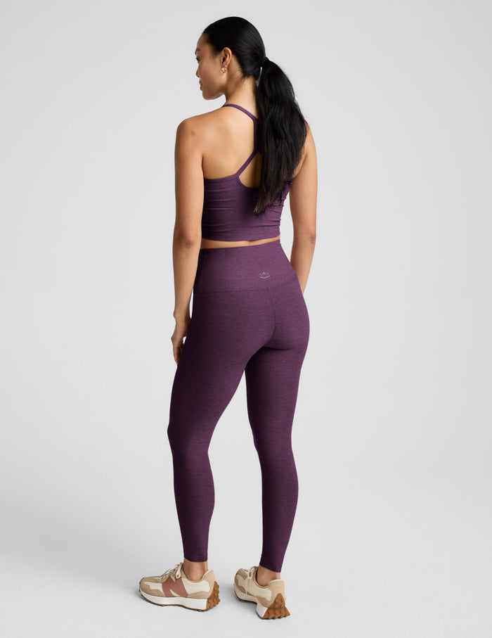 Woman wearing a purple cropped tank and leggings against a plain background.