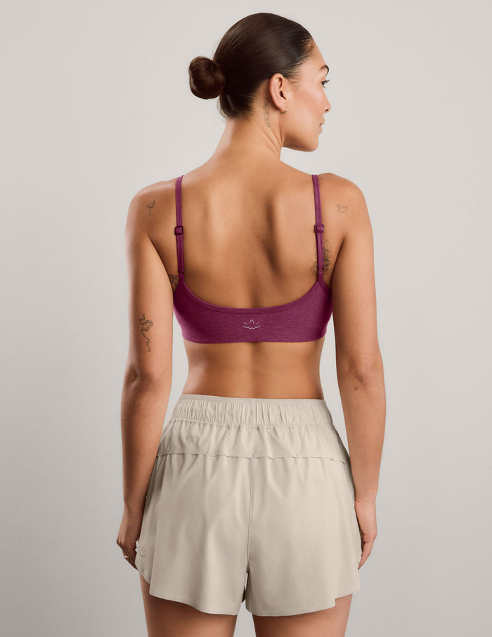 A woman modeling a heathered red purple sports bra and light beige athletic shorts against a solid light gray studio background.