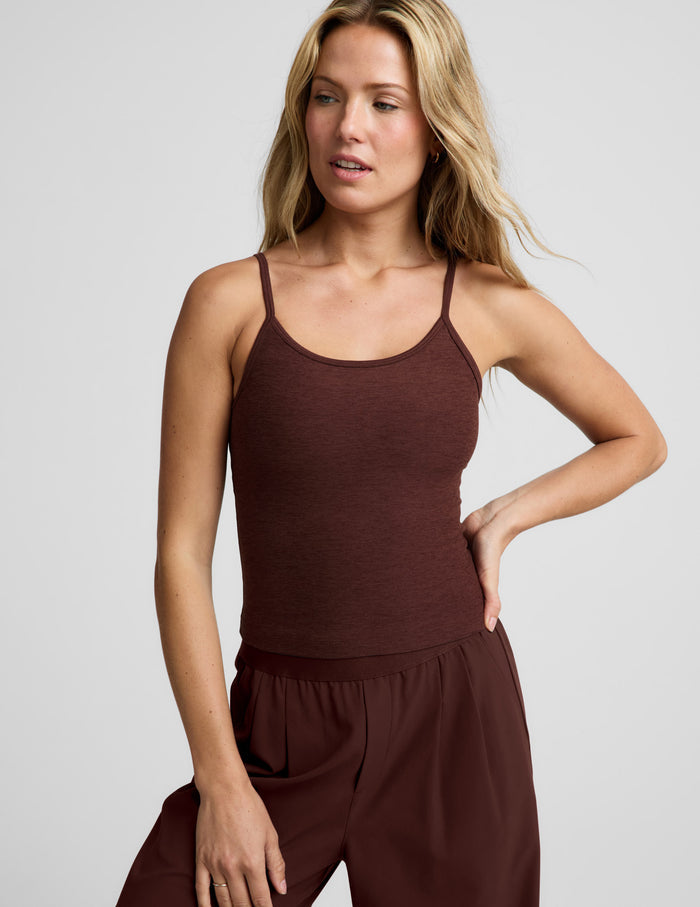 Woman wearing a brown waist length tank top and pants against a plain background.