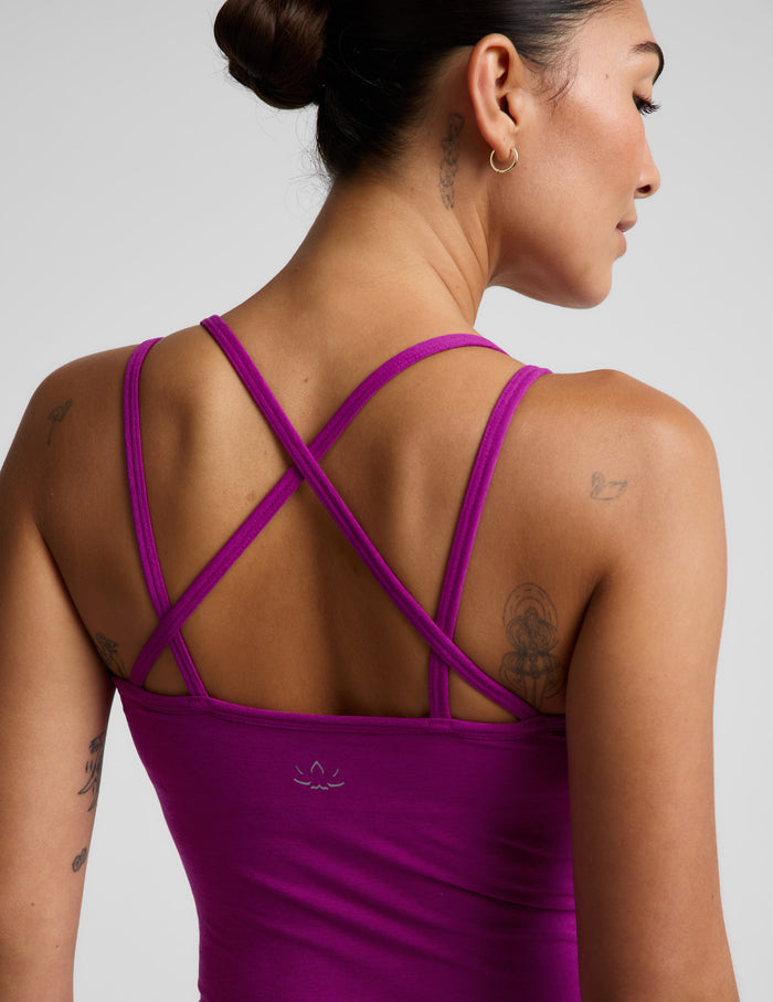 A woman modeling a matching athletic set consisting of a scoop-neck crop tank with a strappy back detail and high-waisted biker shorts in a vibrant magenta-purple color, set against a plain light gray studio background.
