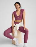 Woman in mauve athletic outfit sitting on a wooden block against a white background.