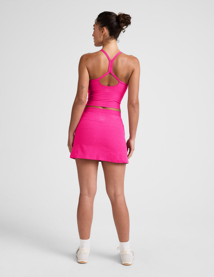 Rear view of a woman in the fuchsia Spacedye Go Pocket Skirt, a high-waisted mini A-line skirt in a bright jewel tone.