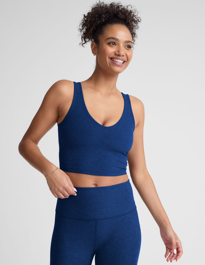 Woman wearing a blue v-neck cropped tank and leggings on a light gray background.