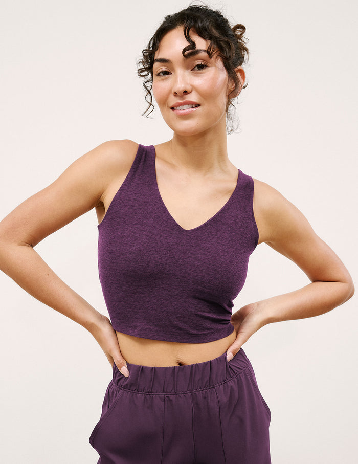 Woman wearing a purple tank top and pants against a plain background.