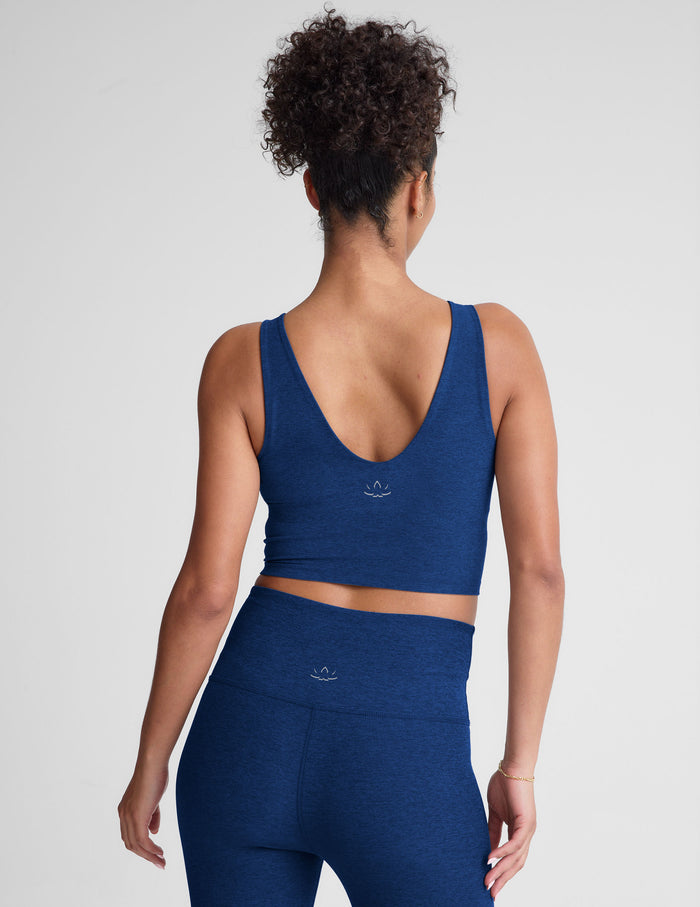 Woman wearing a blue v-neck cropped tank and leggings on a light gray background.