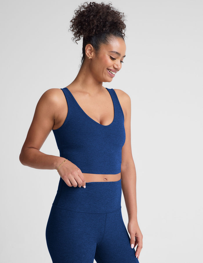Woman wearing a blue v-neck cropped tank and leggings on a light gray background.