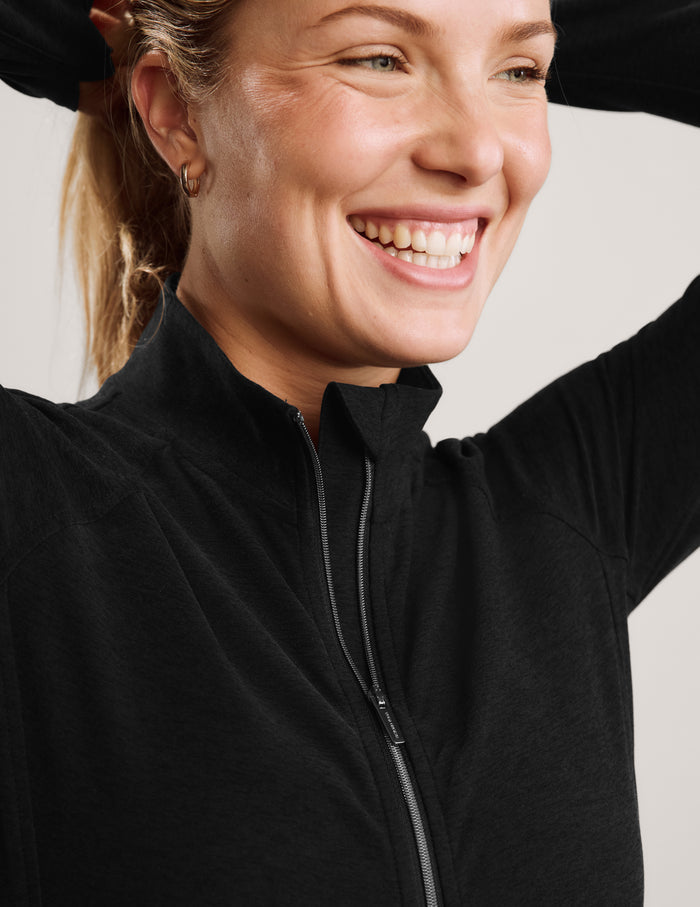 Woman wearing a black full-length zip-up jacket and black biker shorts against a plain background.