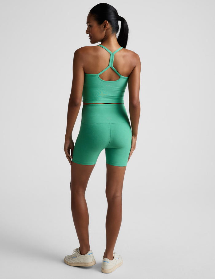 Rear view of a woman in green Spacedye Keep Pace 5" Biker Short and a matching top against a light grey background.