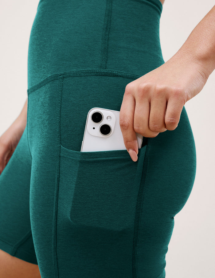 Close-up of a woman placing a phone into the side pocket of the Teal Spacedye™ Keep Pace 5" Pocket Short.
