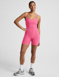 Woman wearing a pink sleeveless biker jumpsuit against a plain background.