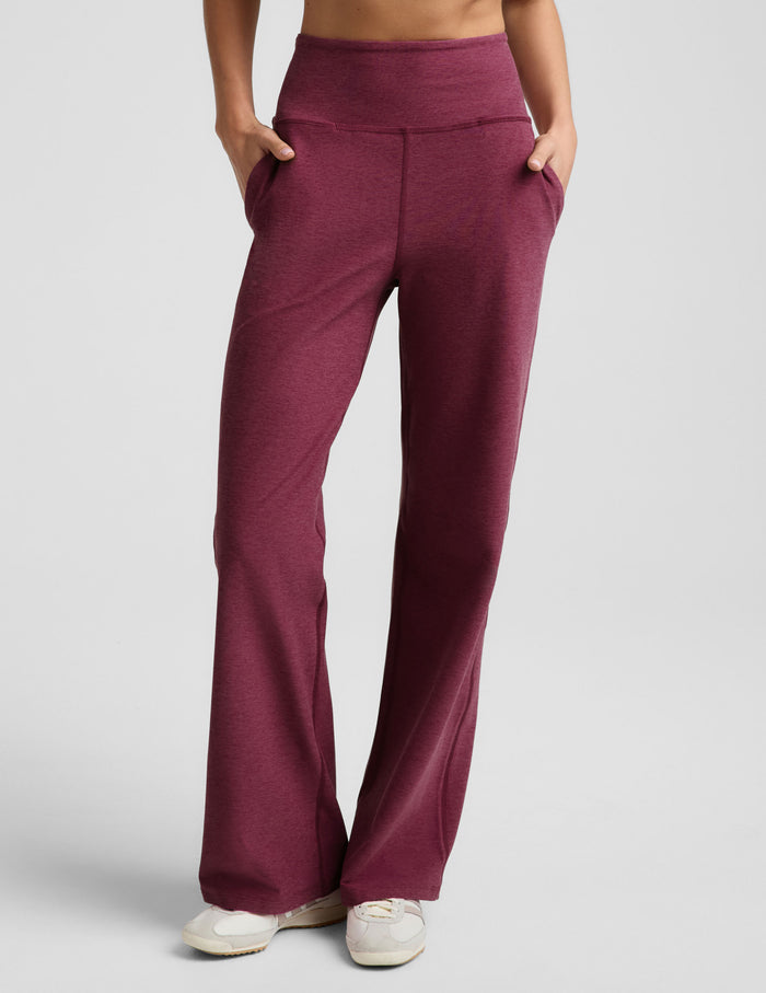 A person wearing heathered burgundy wide-leg lounge pants with side pockets, paired with white sneakers, shown against a light gray studio background.