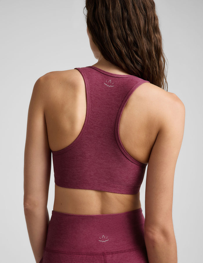 A woman modeling a heathered burgundy sports bra and matching high-waisted pants against a light gray studio background.