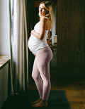 Woman wearing a white maternity tank top and pink maternity leggings with pockets.