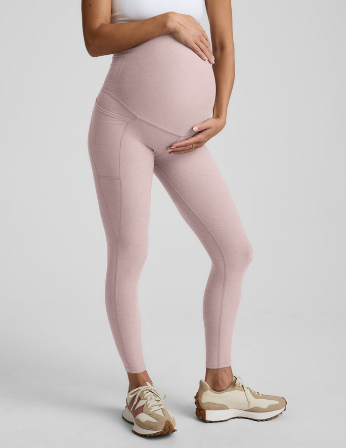Woman wearing pink maternity leggings with pockets against a plain background.