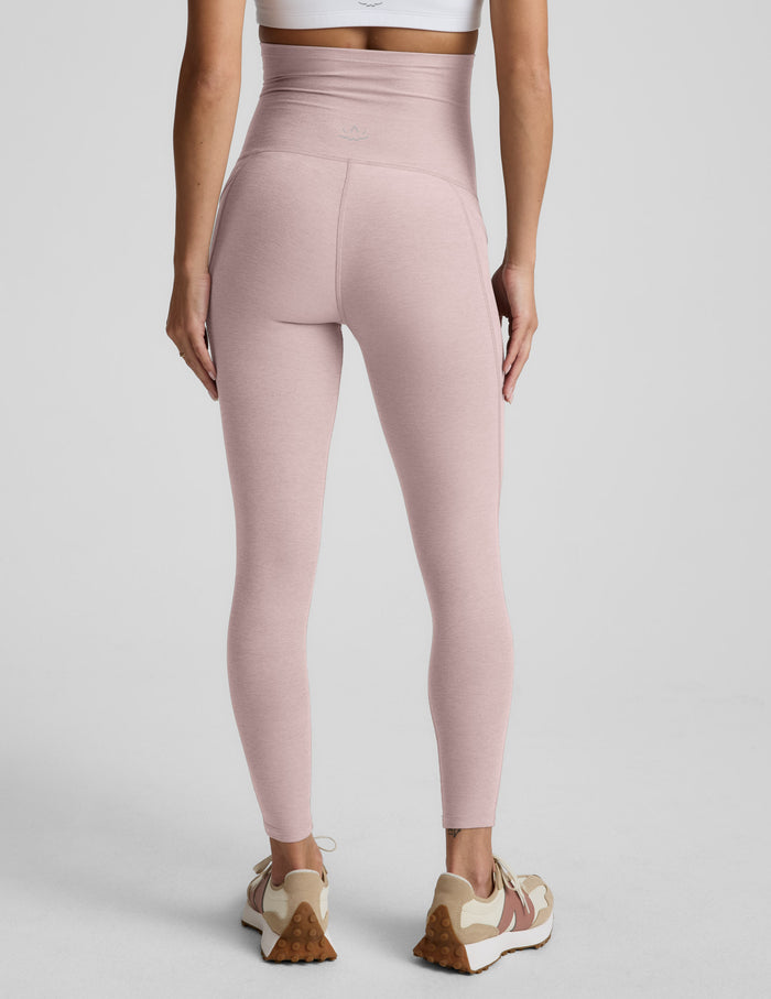 Woman wearing pink maternity leggings with pockets against a plain background.