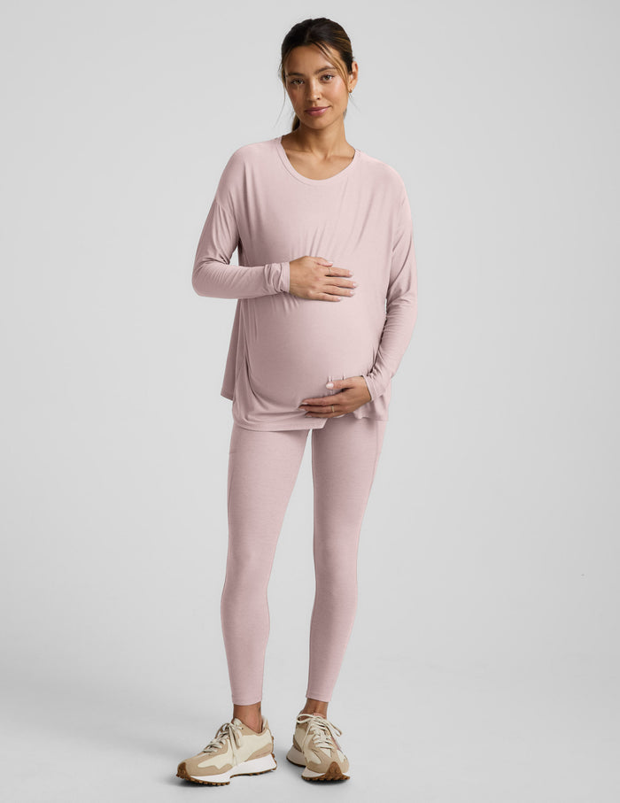 Woman wearing pink long sleeve maternity top and pink maternity leggings with pockets against a plain background.