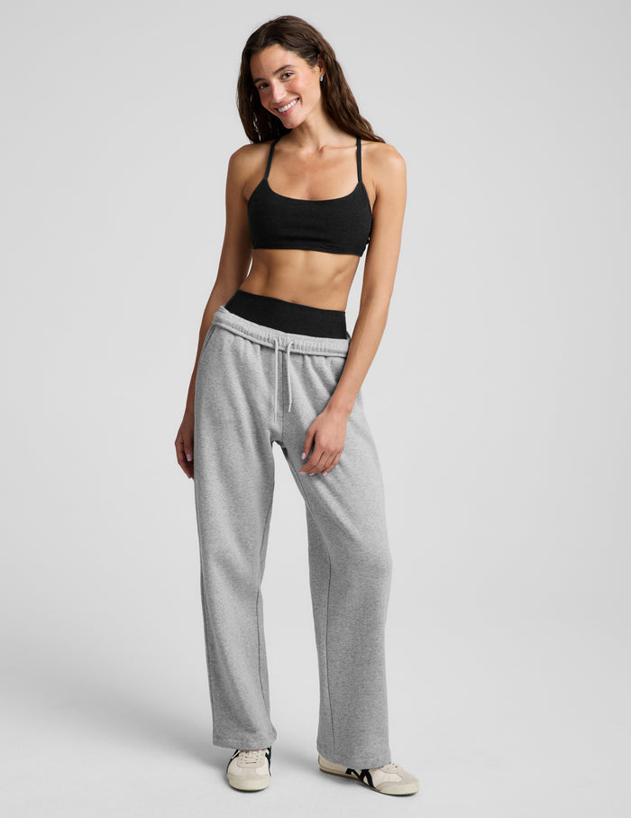 Woman wearing a black bra and gray sweatpants against a plain background.