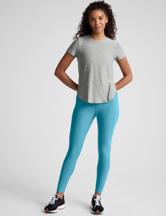 Woman wearing a gray t-shirt and blue leggings on a plain background.
