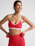 Woman in red sports bra and leggings holding red dumbbells against a light gray background.
