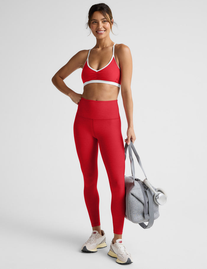 Woman in red athletic outfit holding a gray bag on a light gray background.