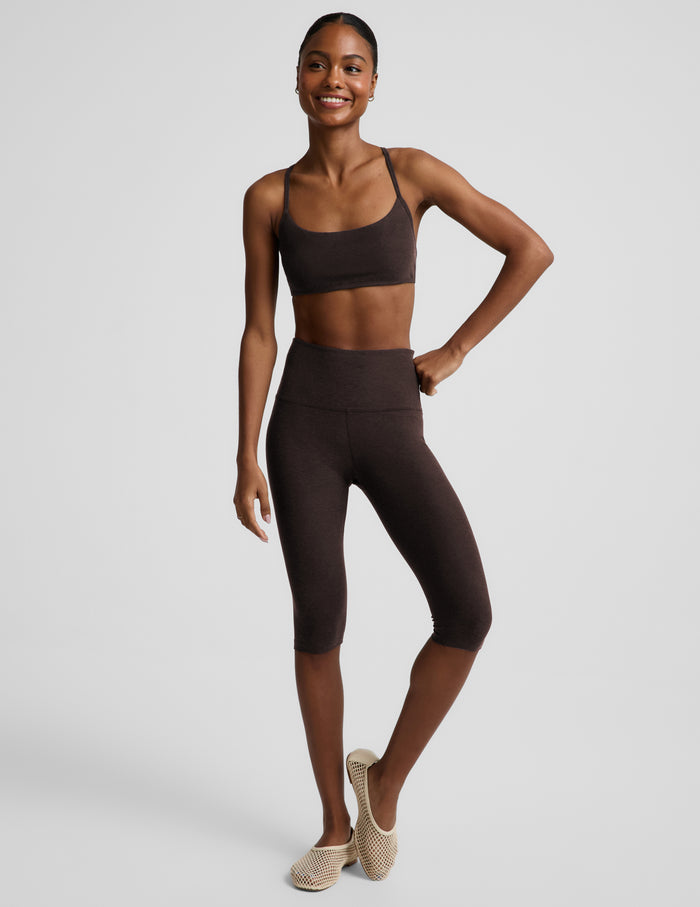 Woman wearing a brown bra and pedal pusher leggings against a plain background.