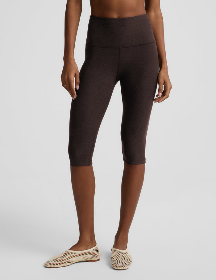 Woman wearing a brown bra and pedal pusher leggings against a plain background.