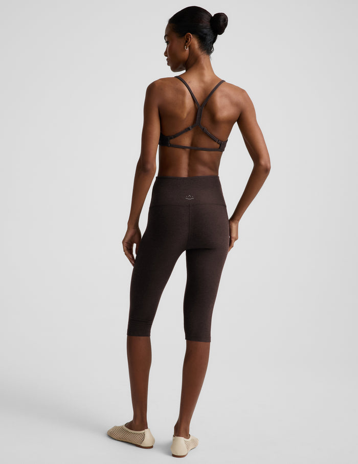 Woman wearing a brown bra and pedal pusher leggings against a plain background.