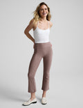 Smiling woman wears brown Spacedye Pintuck Kick Flare High Waisted Pant with front seams and a wide waistband in a studio.