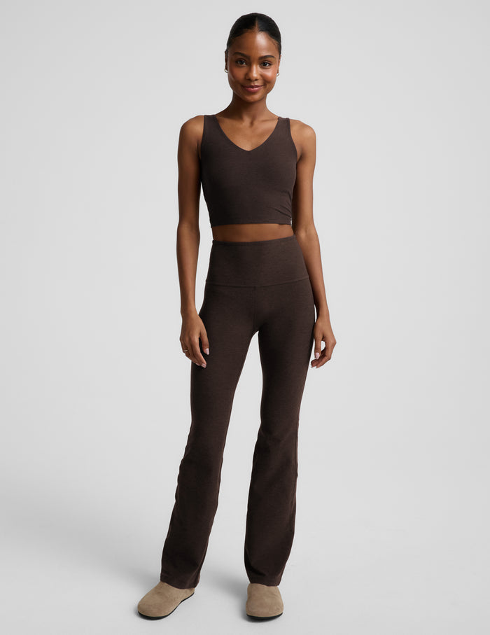 Woman wearing a brown cropped tank top and brown high-waisted bootcut pants against a plain background.
