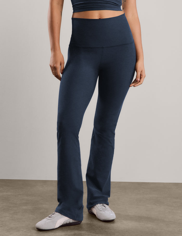 A woman modeling a matching athletic set consisting of a dark navy cropped tank with white trim and high-waisted dark navy blue bootcut pants, standing against a neutral studio backdrop.