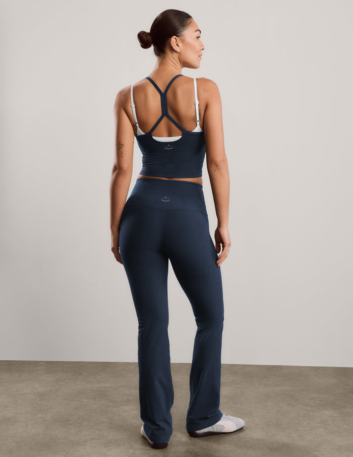 A woman modeling a matching athletic set consisting of a dark navy cropped tank with white trim and high-waisted dark navy blue bootcut pants, standing against a neutral studio backdrop.