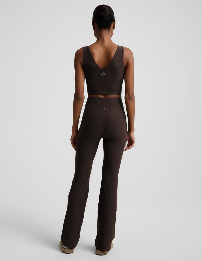 Woman wearing a brown cropped tank top and brown high-waisted bootcut pants against a plain background.
