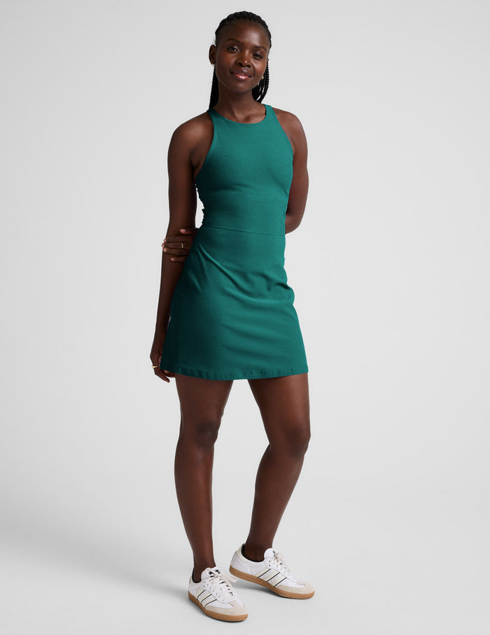 Woman wearing a green high-neck racerback mini dress against a plain background.