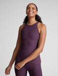 Woman wearing a purple sleeveless top and leggings on a plain background.