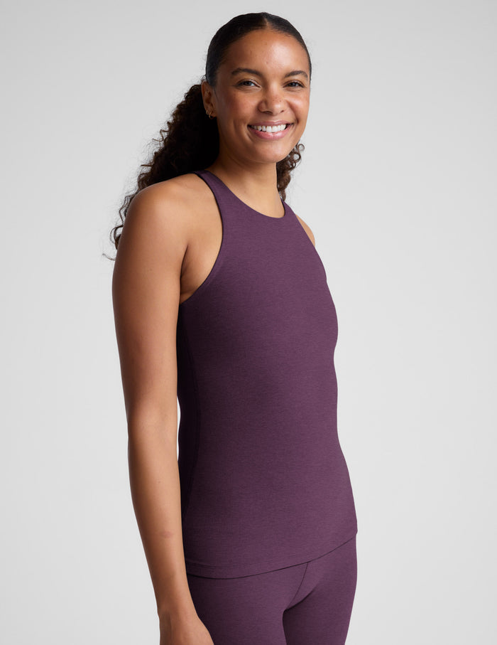 Woman wearing a purple sleeveless top and leggings on a plain background.